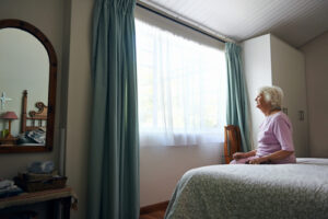 Elderly woman alone in nursing home looking outside a window